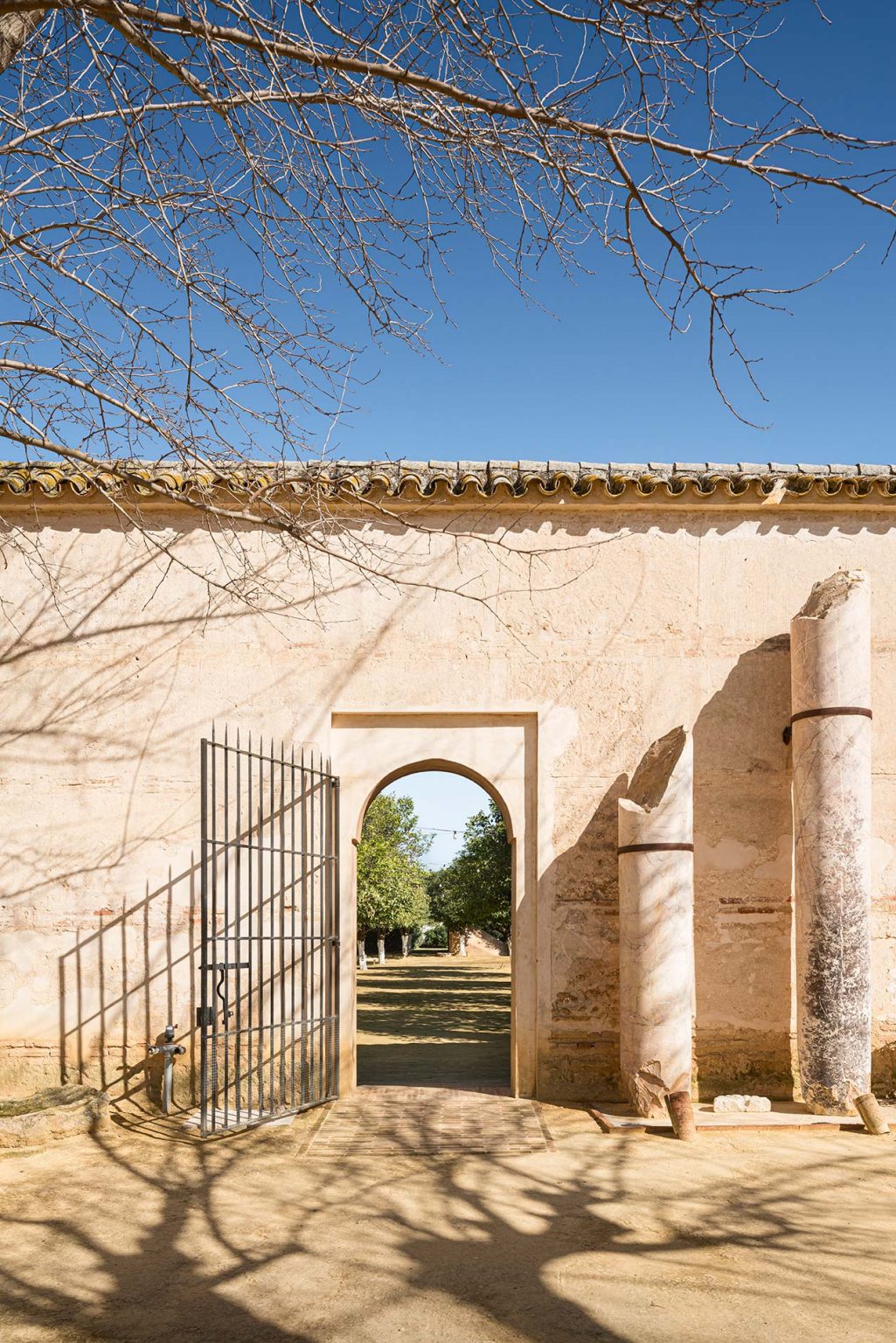 Muro encalado con puerta de arco apuntado, verja de hierro y columnas caídas
