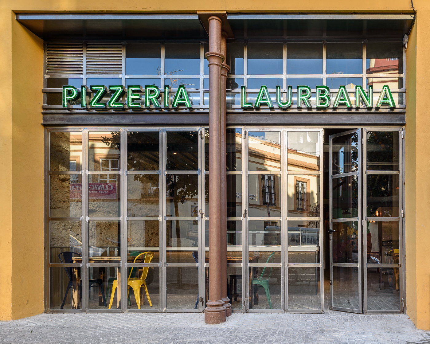 Fachada de la pizzería La Urbana con rótulo de neón verde y carpintería de acero