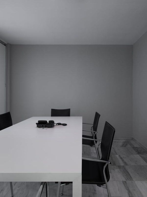 Sala de reuniones gris con mesa blanca alargada, sillas negras y un teléfono