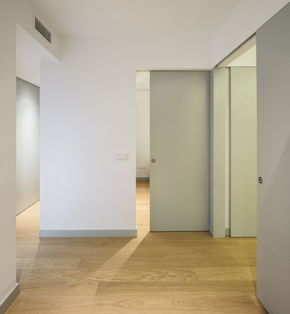 Pasillo de paredes blancas con puertas correderas y suelo de madera clara