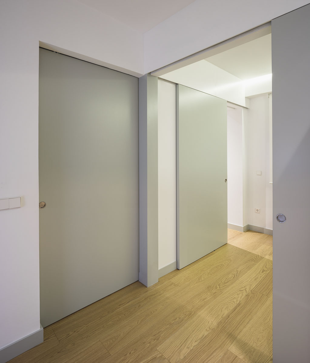 Pasillo con puertas correderas verde claro y suelo de madera clara