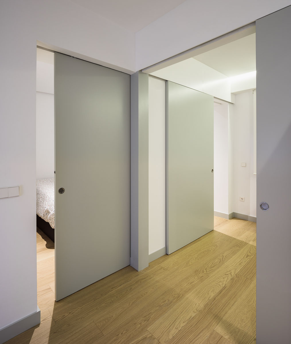 Pasillo con puertas correderas y suelo de madera, con un dormitorio al fondo izquierda
