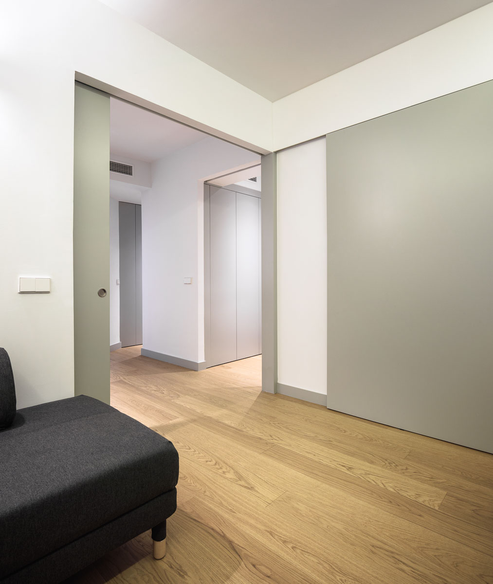 Puerta corredera verde claro abierta al pasillo, con suelo de madera