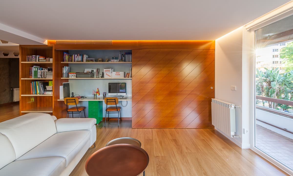 Salón con panel corredero de madera que oculta una zona de estudio con estanterías