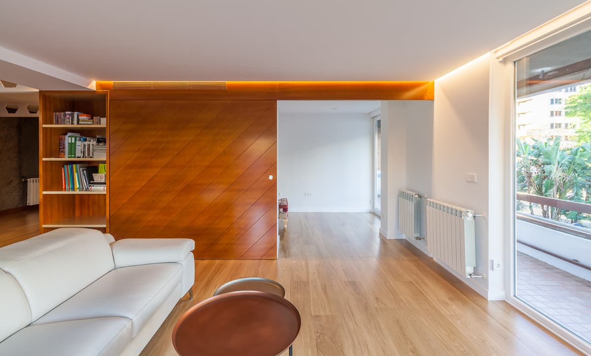 Salón con sofá blanco, panel de madera y ventanal a la terraza