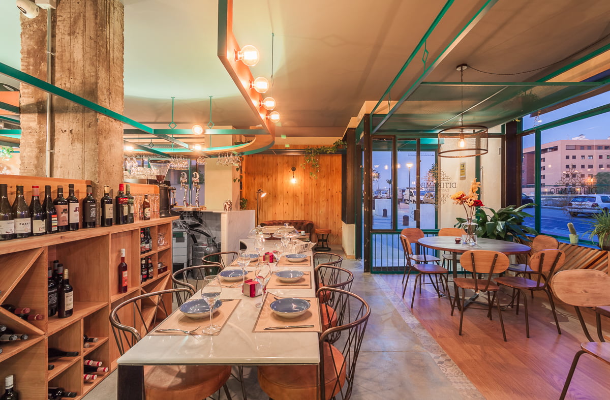 Mesa larga junto al botellero de madera, con tuberías verdes vistas en el techo
