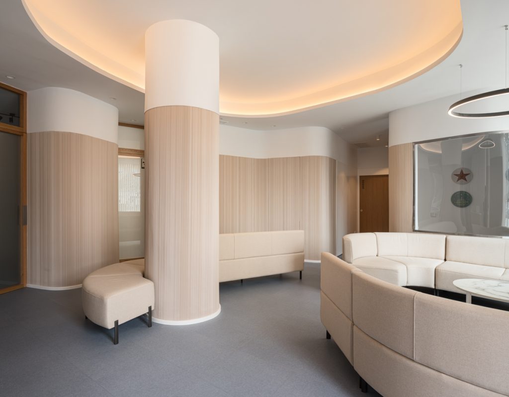 Sala de espera con pilar revestido de madera y sofá curvo, en la Clínica Dental Vilches