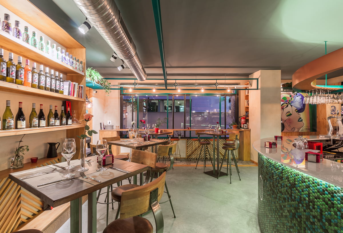 Comedor con estantería de botellas, barra de mosaico verde y conductos vistos