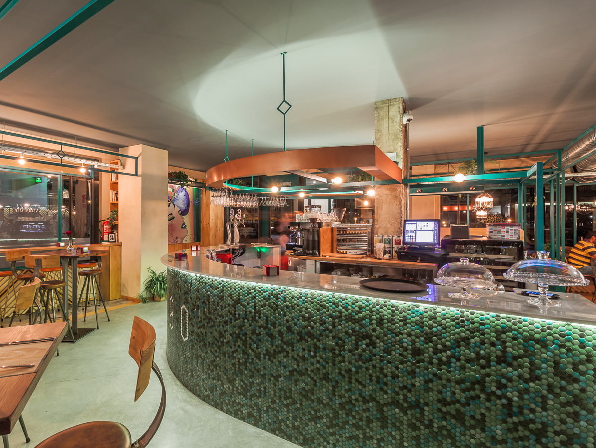 Barra curva revestida de mosaico verde bajo la estructura metálica del comedor