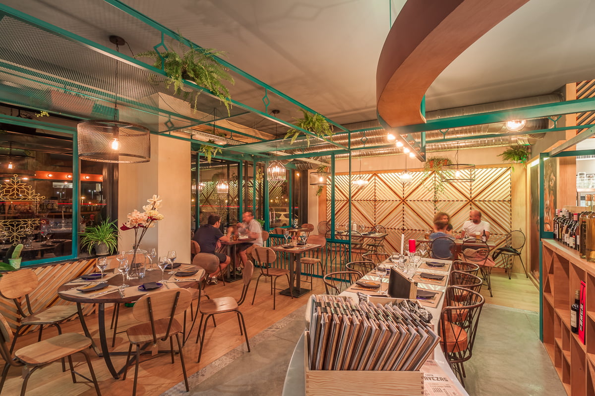 Comedor del restaurante con estructura verde, plantas colgantes y clientes en las mesas