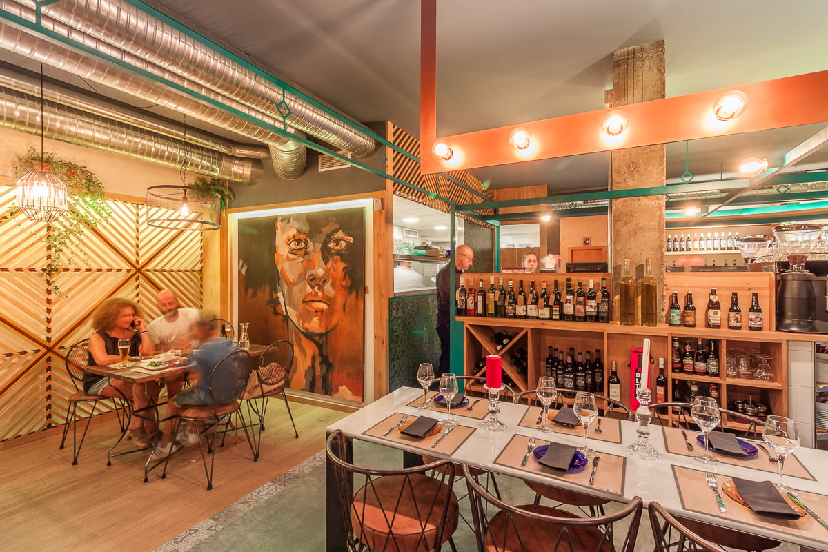 Interior del restaurante con mural de un rostro, botellero y mesas puestas