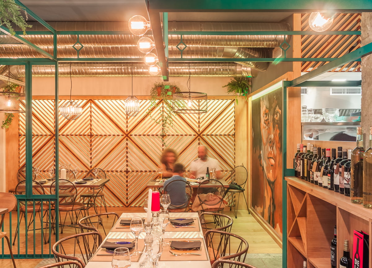 Comedor con estructura metálica verde, celosía de madera y mural de un rostro