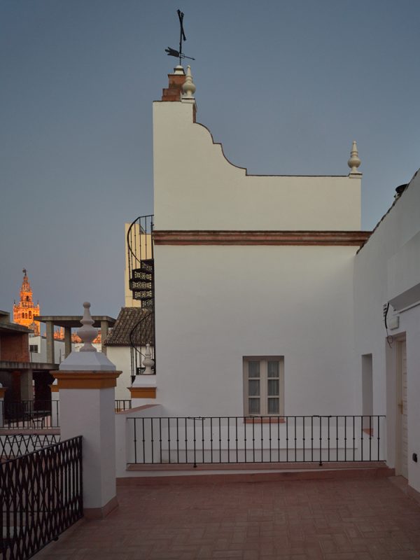 Azotea al atardecer con la Giralda al fondo y una veleta sobre el remate blanco