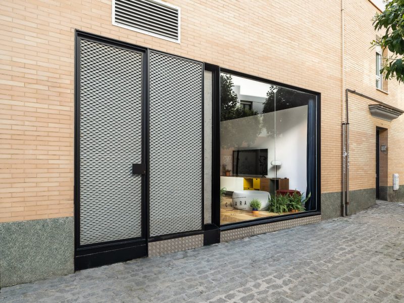 Fachada de ladrillo con escaparate y puertas de chapa estirada sobre calle adoquinada