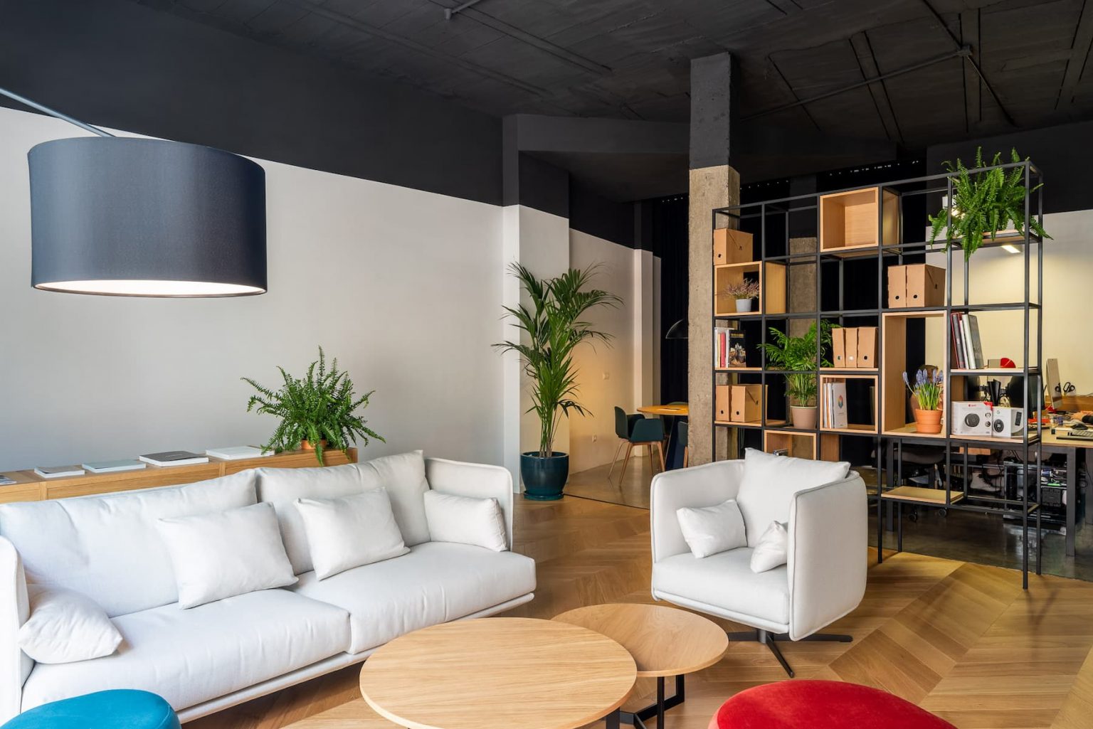 Sala de espera con sofás blancos, pufs de colores y estantería metálica, en Clara Hábitat