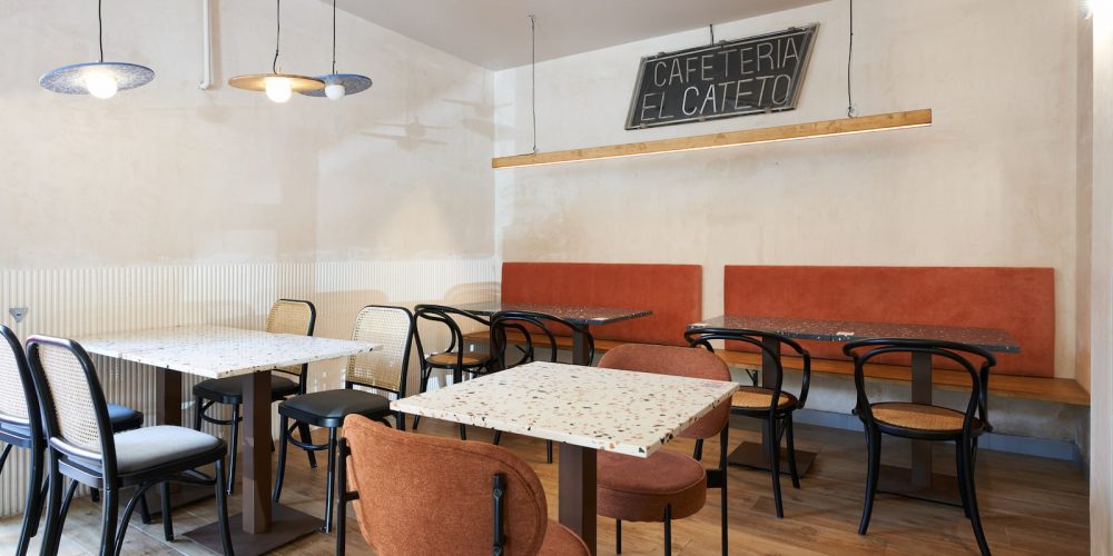 Comedor del bar con mesas de terrazo, sillas de rejilla y banco tapizado naranja