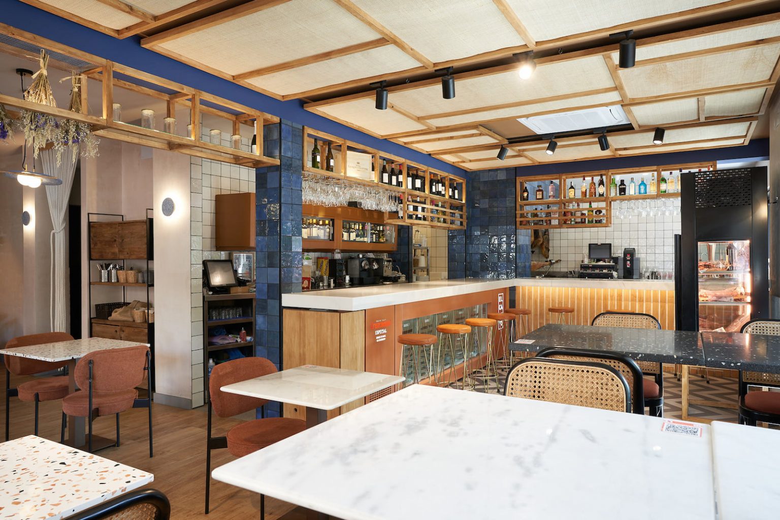 Sala con barra de mármol, azulejo azul y techo de listones, en el bar El Cateto