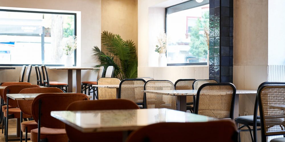Sala del bar con butacas naranjas, sillas de rejilla y mesas de terrazo