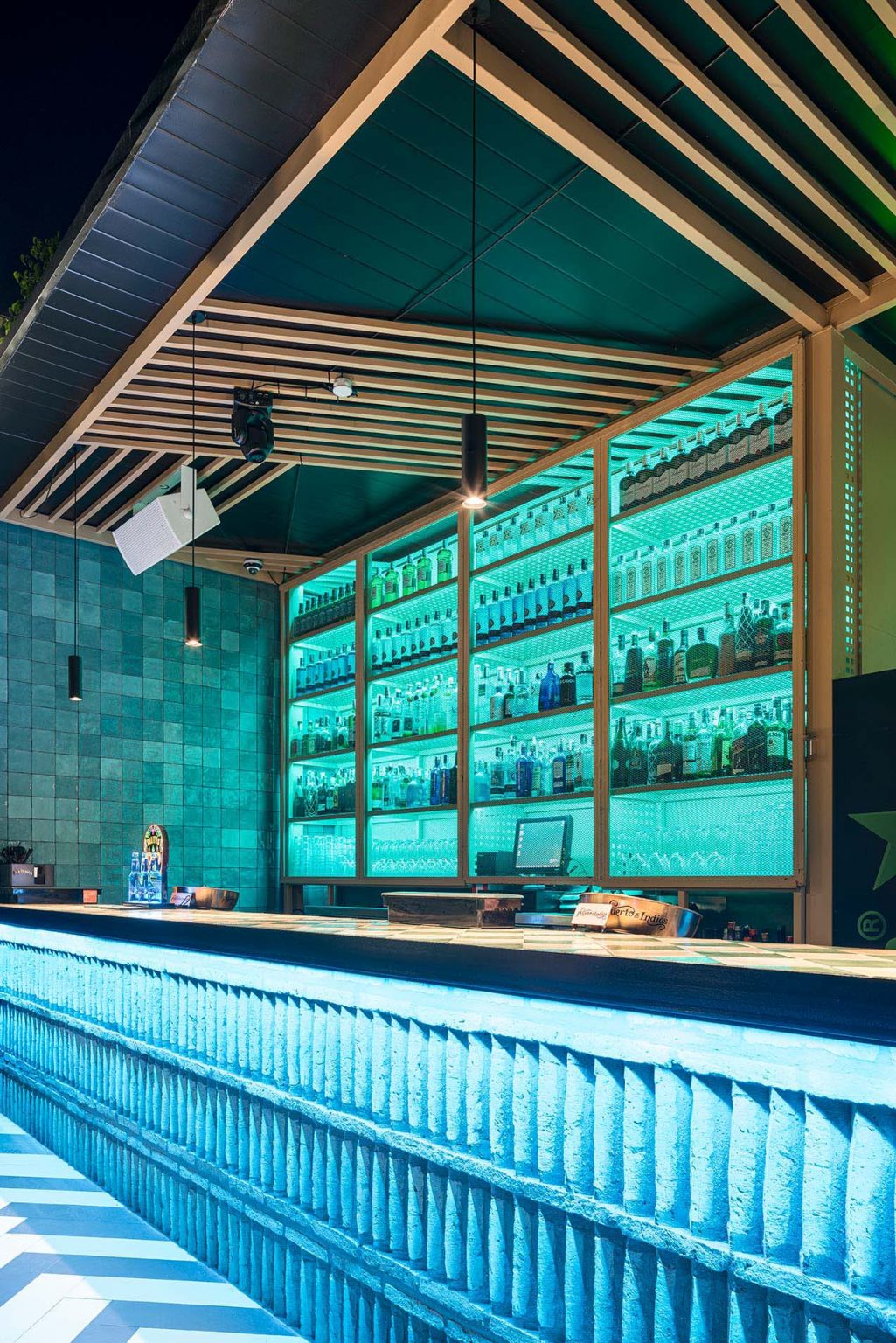 Barra exterior de noche con luz turquesa y estantería de botellas retroiluminada