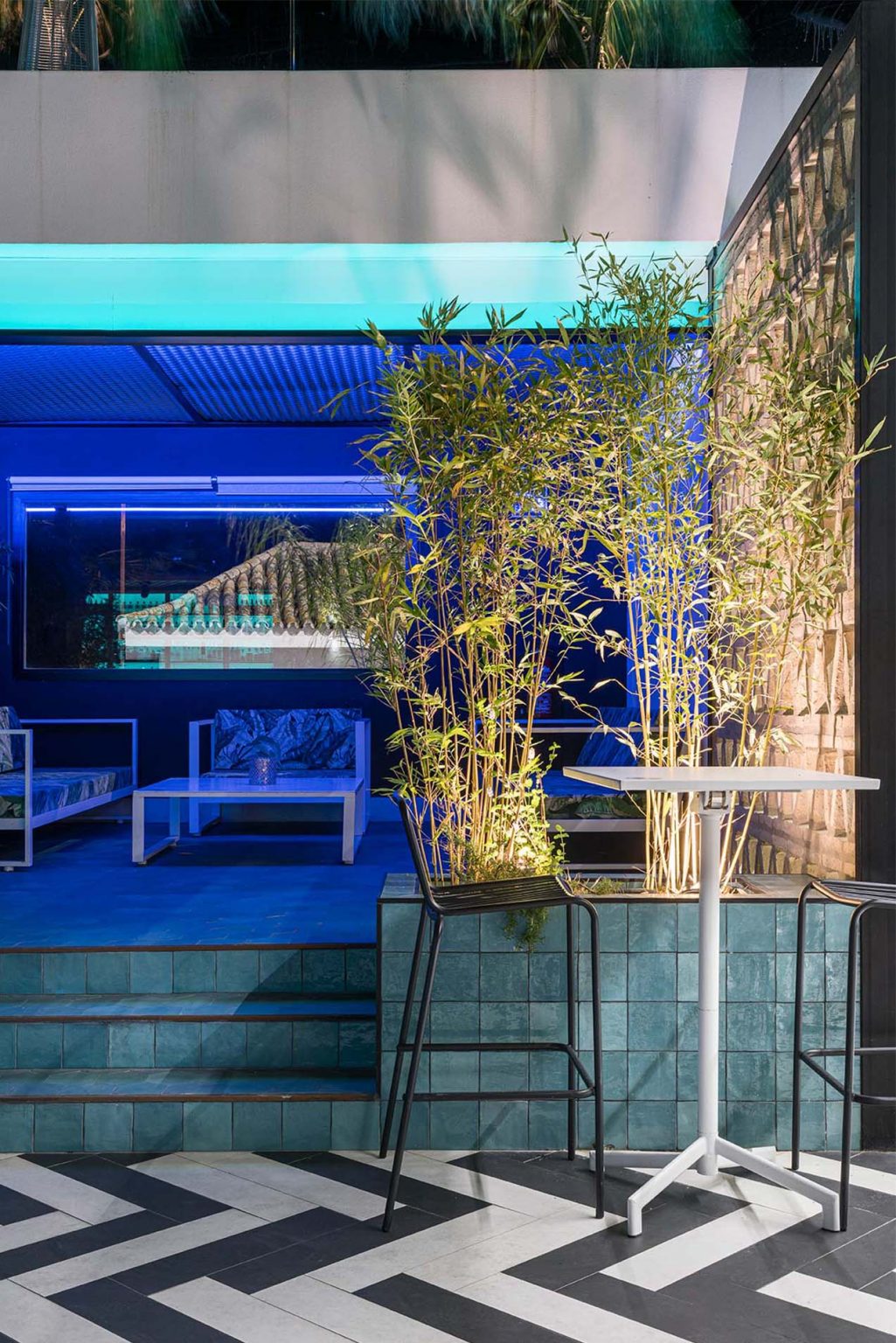 Terraza de noche con iluminación azul, cañas de bambú y suelo en espiga