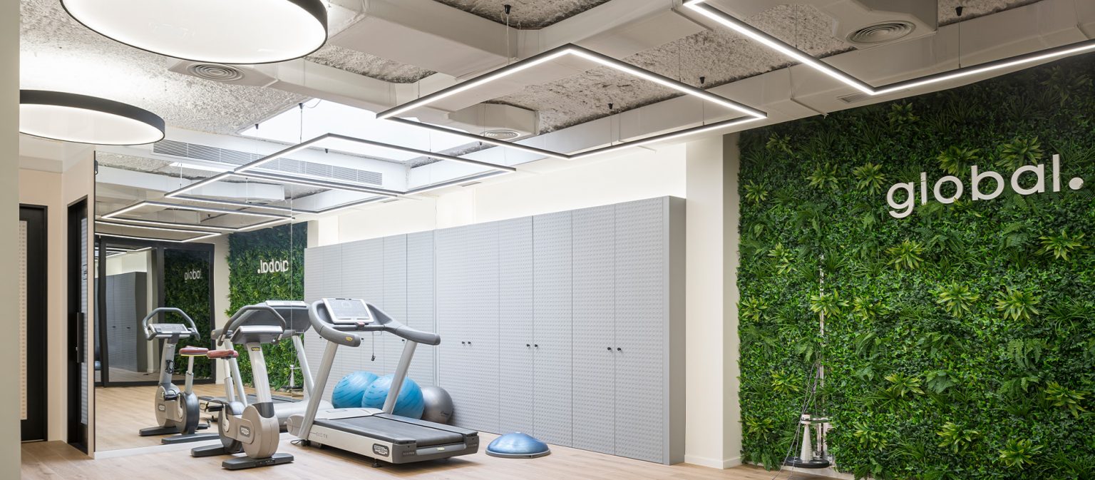Sala de fitness con cintas de correr frente a un jardín vertical rotulado global