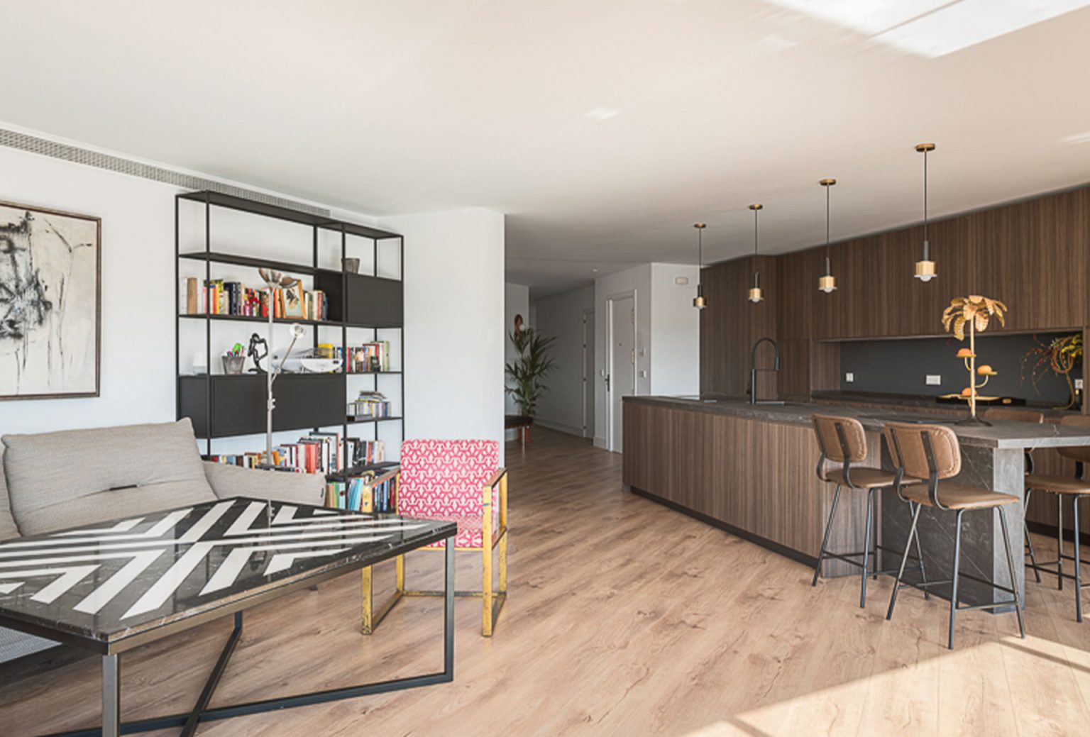Salón con estantería negra abierto a la cocina con isla de madera y taburetes
