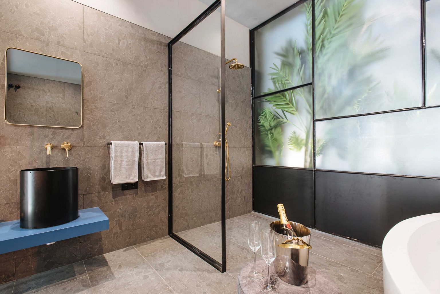 Baño con ducha de vidrio, lavabo negro sobre repisa azul y bañera exenta