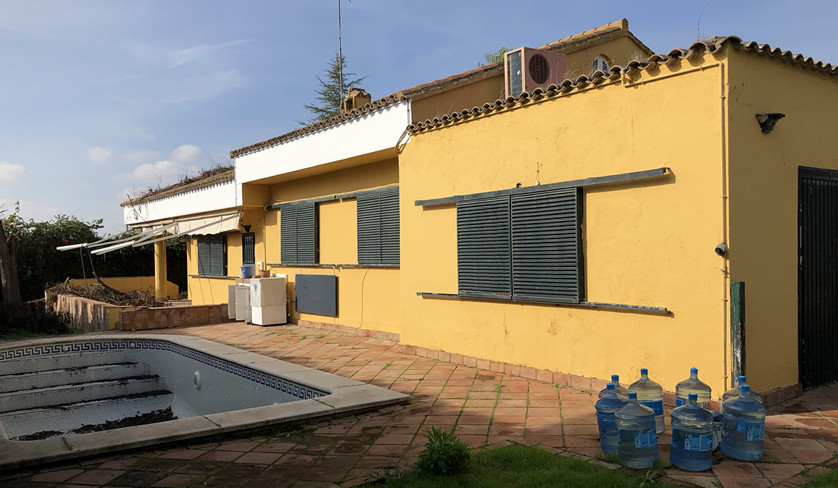Casa de fachada amarilla con persianas bajadas y una piscina sin limpiar