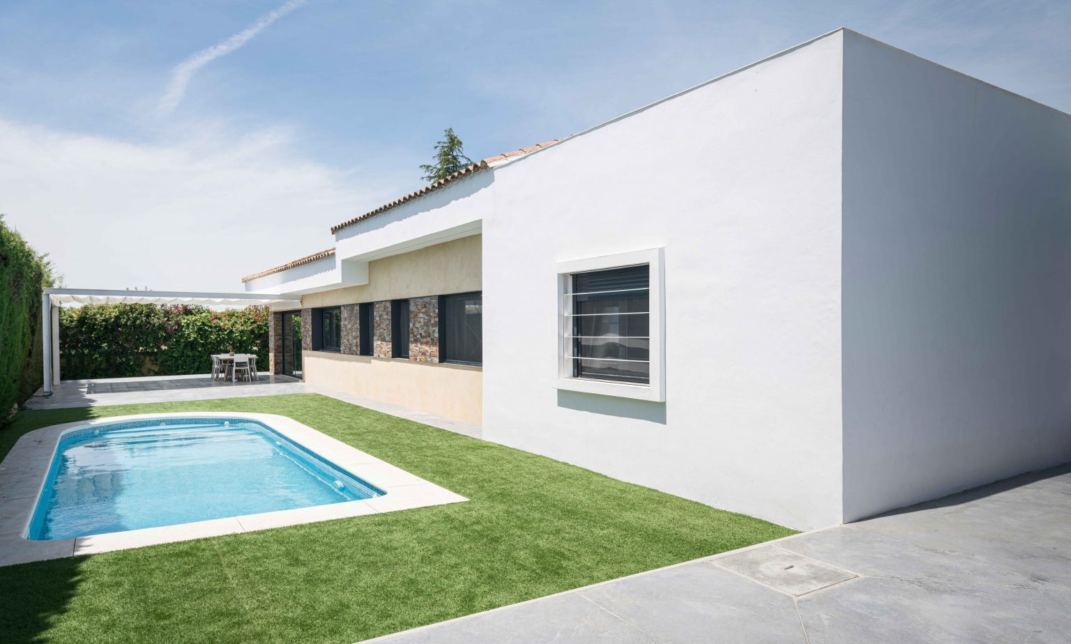 Piscina y césped junto al volumen blanco de la casa de Espartinas