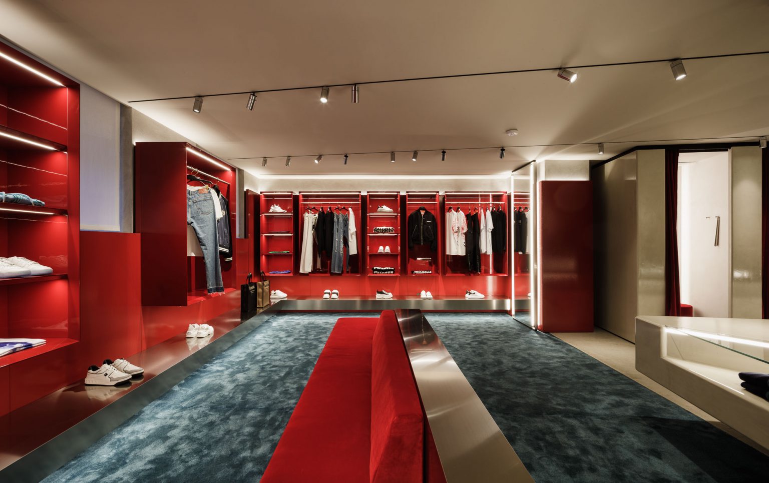 Tienda de ropa con paredes rojas, expositores iluminados, moqueta azul y banco central