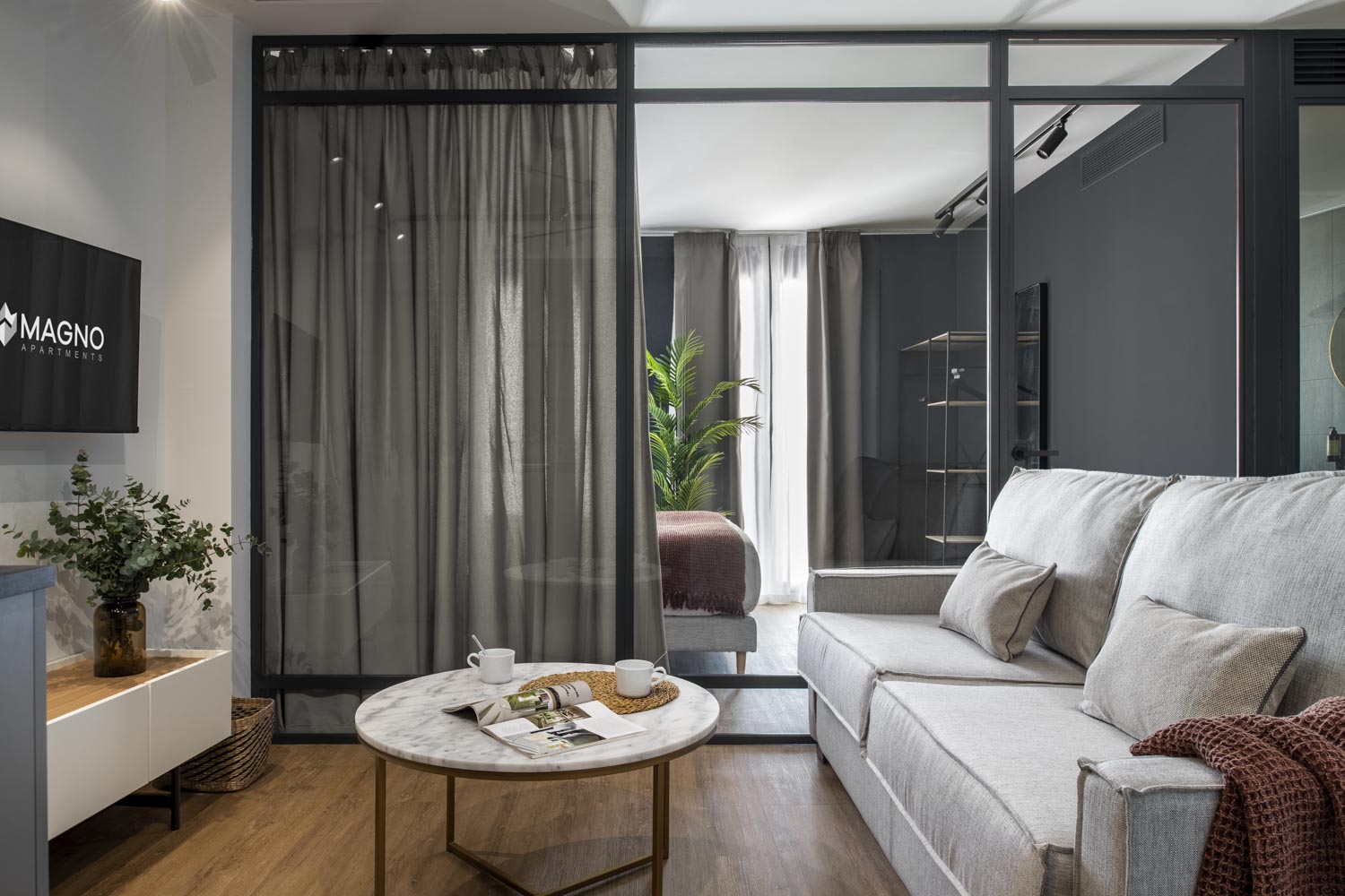 Salón con sofá gris, mesa baja redonda y dormitorio tras cortina y carpintería negra