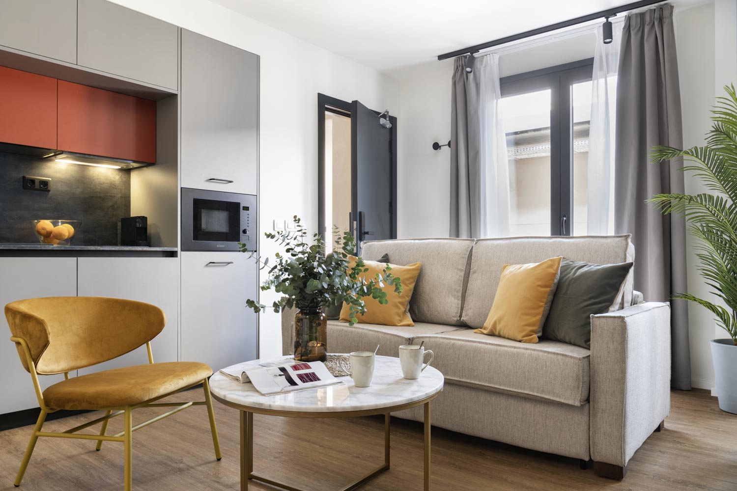 Salón con cocina integrada, sofá beige, butaca amarilla y mesa redonda de mármol