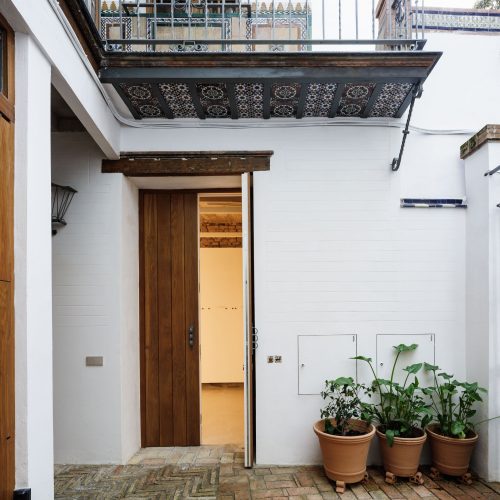 Patio encalado con puerta de madera abierta, macetas de barro y suelo de ladrillo