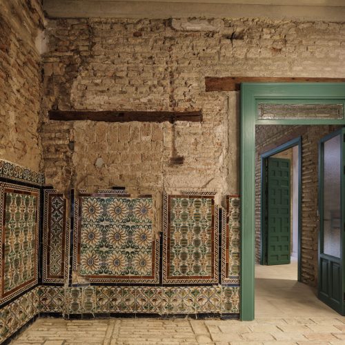 Detalle del muro de ladrillo descarnado con el zócalo de azulejos y la puerta verde