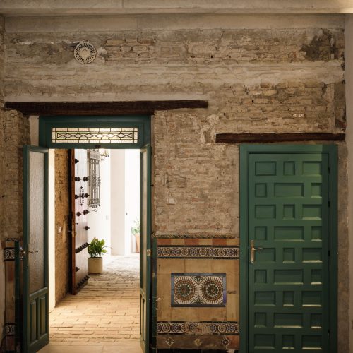 Zaguán con puertas verdes de madera, muro de ladrillo antiguo y zócalo de azulejos