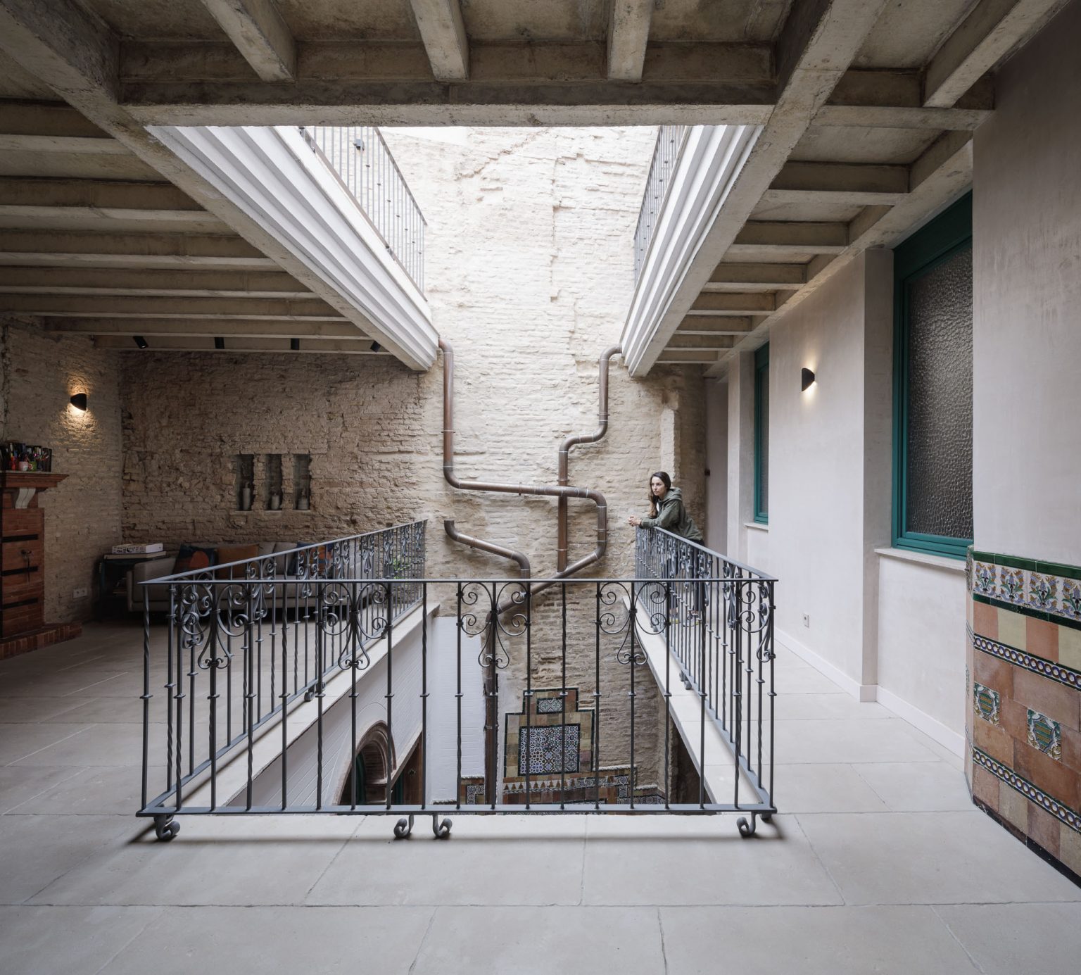 Galería sobre el patio con vigas vistas, muro de ladrillo y barandilla de forja