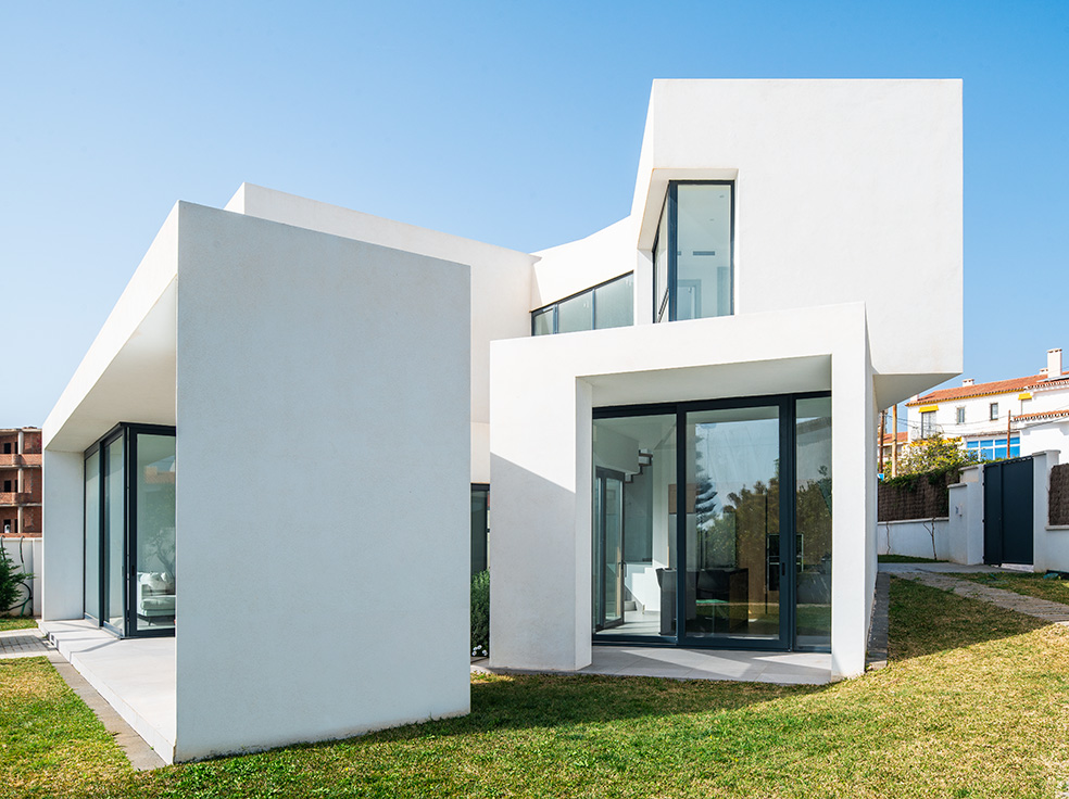 Exterior de vivienda blanca de volúmenes escalonados con grandes ventanales al jardín