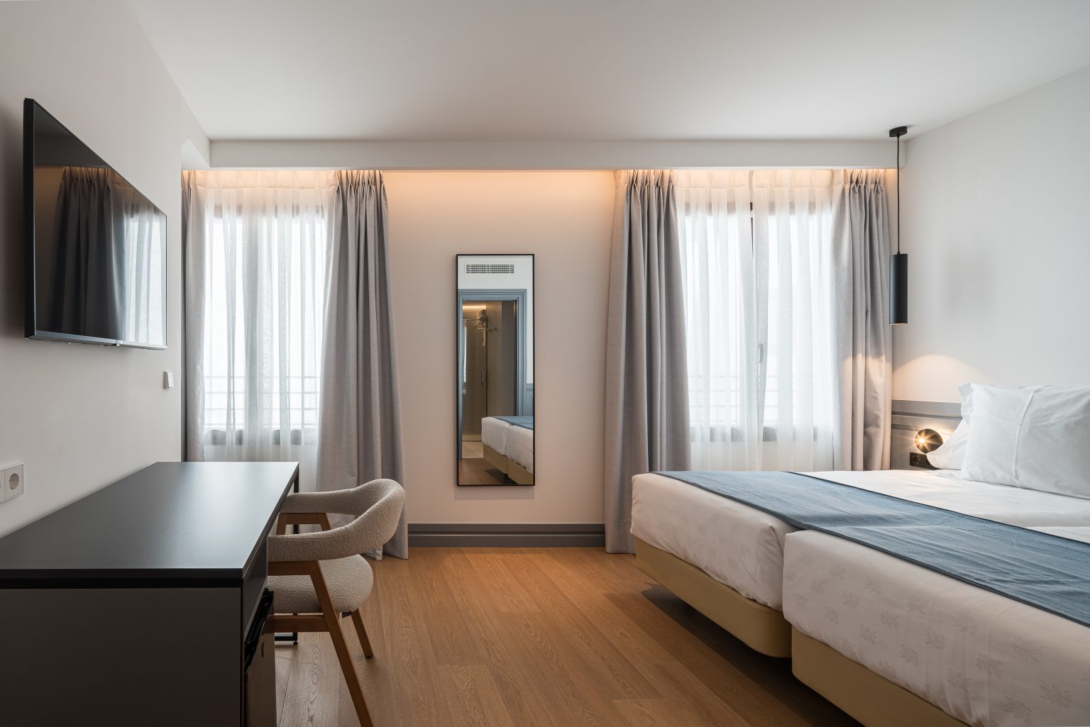 Habitación con escritorio, espejo y colcha azul, en el Hotel Reinoso