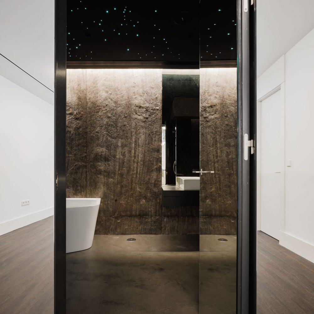 Baño con bañera exenta, paredes texturizadas oscuras y techo negro con puntos de luz